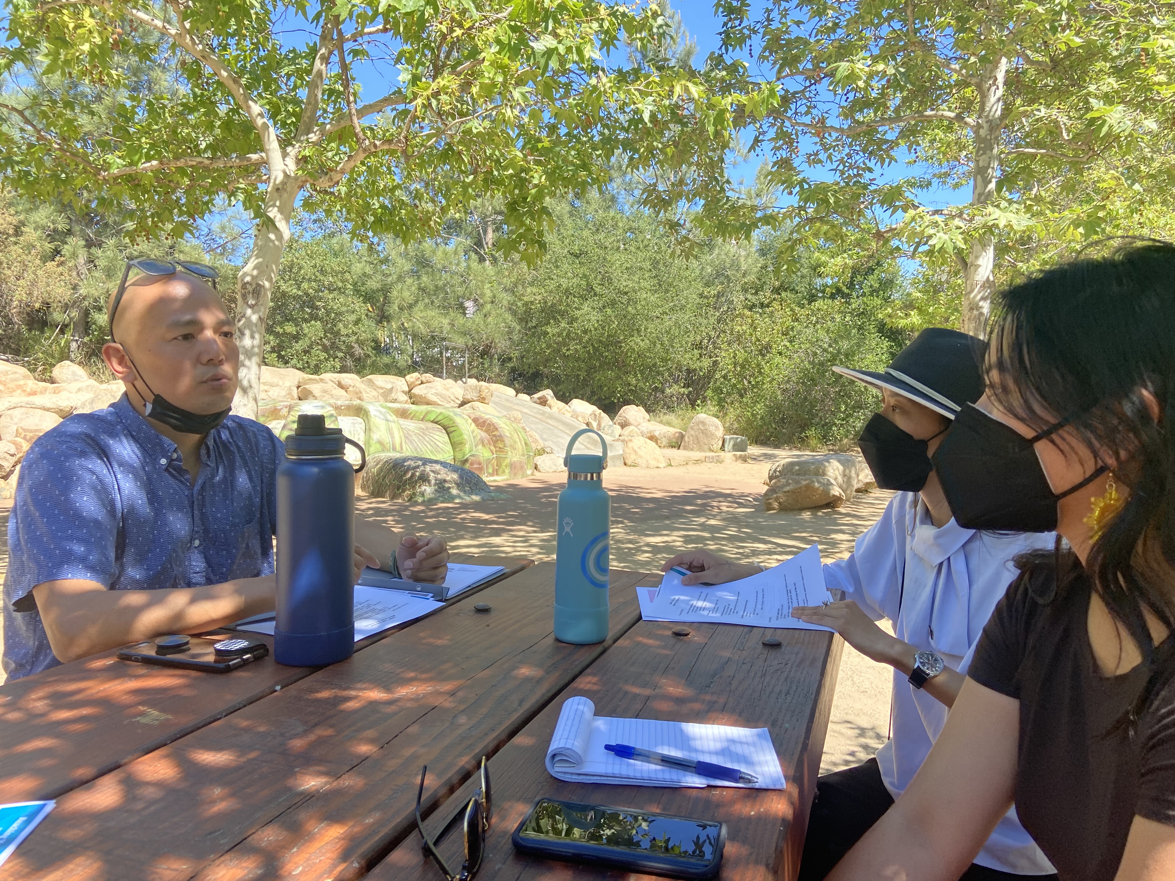 several people sit around a picnic table with masks on